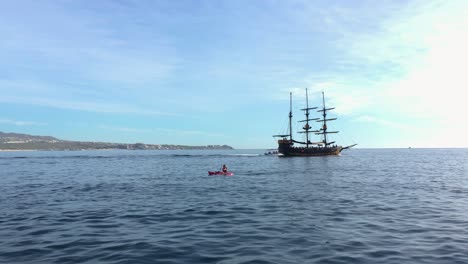 Gente-Navegando-En-Kayak-En-El-Mar-Frente-A-Un-Barco-Pirata-En-Un-Día-Soleado-En-Cabo-San-Lucas,-México