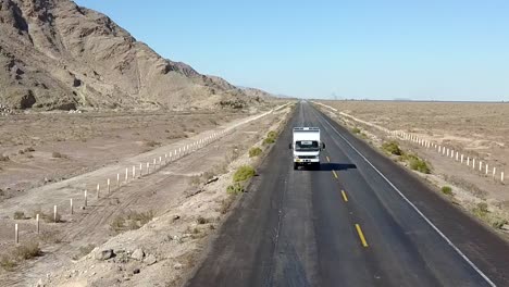 Aerial,-reverse,-drone-shot,-in-front-of-a-camper-rv,-truck,-driving-on-a-desert-road,-on-a-sunny-day,-on-San-Felipe-highway,-in-Baja,-California,-Mexico