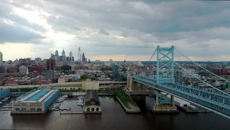 Aerial-Drone-flying-over-the-Delaware-River-to-show-the-Ben-Franklin-Bridge-and-the-Philadelphia-skyline-surrounded-by-sun-and-clouds