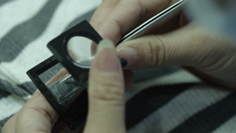 Close-up-on-hands-of-a-female-factory-worker-doing-a-quality-check-of-textile-sample-with-magnifying-glass-and-removing-pellets-with-tweezers,-China,-Asia