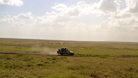 Safari-tour-car-driving-on-the-road-through-Serengeti-National-park-on-a-sunny-day-,-with-beautiful-big-clouds-over-horizon,-Tanzania