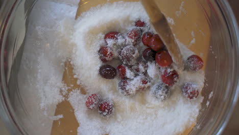 Slow-motion-overhead-wooden-spoon-mixing-and-stirring-fresh-red-cranberries-and-white-sugar-in-clear-glass-bowl