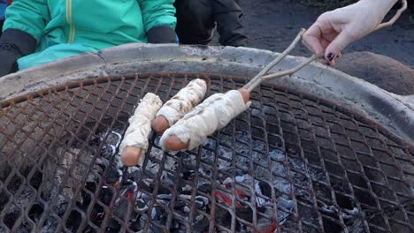 Barbecuing-stick-bread-on-hot-dogs,-on-a-cold-winters-day
