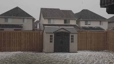 Crane-shot-moving-upwards-showing-a-residential-backyard-during-a-winter-snowfall