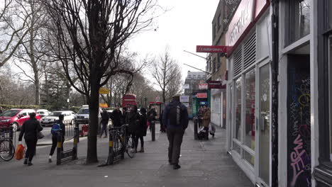 UK-February-2019---People-walking-and-cycling-past-shops-on-a-tree-lined-high-street-pavement