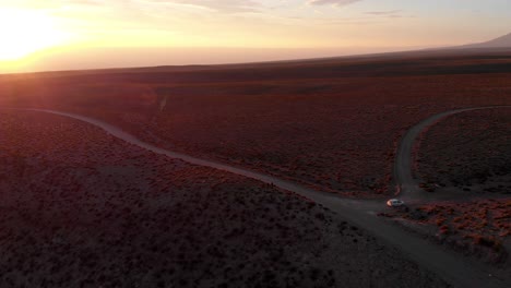Aerial-cinematic-shot-of-two-travelers-on-a-dirt-road-at-sunset-in-the-Atacama-Desert,-Chile,-South-America