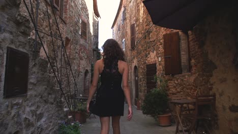 A-young-brunette-woman-in-a-black-dress-is-walking-through-a-little-medieval-Italian-village