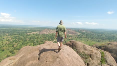 Slow-motion-shot-tracking-a-bearded-ginger-man-with-a-large-hat-as-he-climbs-on-a-large-granite-boulder-with-views-of-the-East-African-landscape