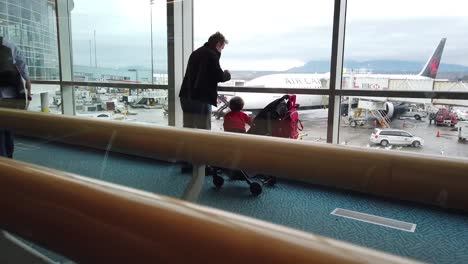 A-man-and-a-child-looking-out-the-window-at-an-airport-and-seeing-an-Air-Canada-aircraft