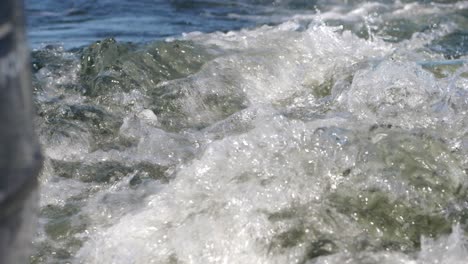 Blue-ocean-wake-foam-moving-behind-boat-motor-in-slow-motion,-shallow-depth-of-field