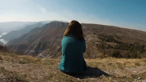 Mädchen,-Das-An-Einem-Sonnigen-Tag-Auf-Einem-Berg-Sitzt,-Mit-Wunderschönem-Canyonsee-Im-Hintergrund