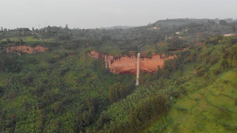 A-pulled-back-panning-aerial-shot-of-sipi-falls-pouring-over-the-edge-of-a-cliff-in-rural-Africa