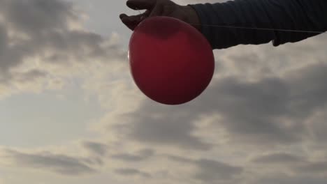 Hält-Einen-Roten-Ballon-Gegen-Wolkengebilde