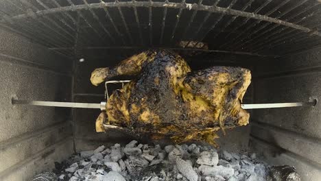 Rotisserie-Chicken-rotating-in-a-wood-and-charcoal-fire-brick-bbq-grilling-in-slomo