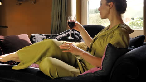 Classy-white-caucasian-woman-sitting-down-in-couch,-relaxing,-holding-a-glass-of-wine,-slow-motion