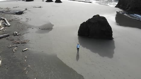 Drone-follows-guy-on-beach-walking-toward-sea-stack