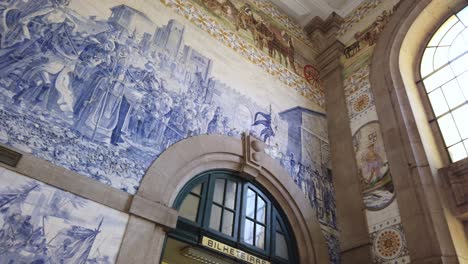 Pan-right-to-view-blue-and-white-azulejo-tile-art-adorning-upper-walls-inside-Sao-Bento-Station,-Porto,-Portugal
