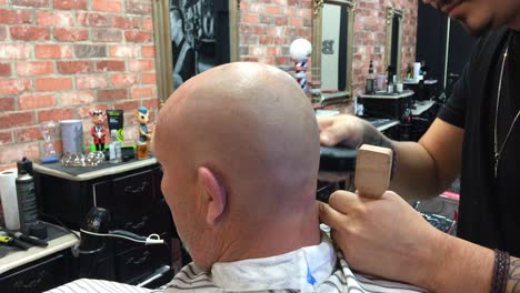 Adult-Male-at-a-retro-style-barbershop-having-his-hair-shaved-off-by-a-professional-barber-using-a-clipper-machine-gloves-customer