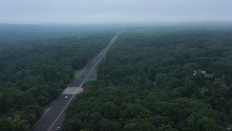 Aerial-footage-travels-over-the-trees-alongside-a-suburban-highway-into-the-morning-fog