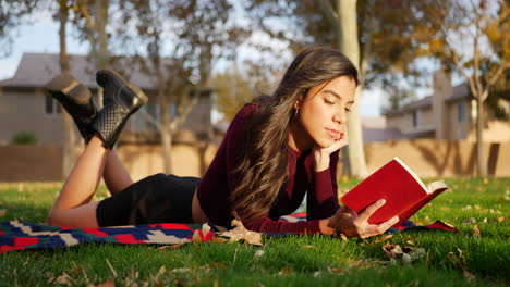Attractive-young-hispanic-woman-college-student-reading-a-book-outdoors-in-the-park-before-class-starts-in-the-fall-semester