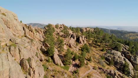 Drone-shot-of-mountainous-terrain,-hikers-and-cityscape-in-the-distance