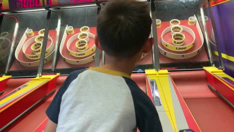 Camera-focusing-on-a-young-boy-playing-skee-ball-at-an-arcade