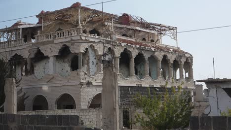 Panning-shot-across-the-street-of-Syria-Damascus-passing-trees-and-ruined-buildings-due-to-civil-war