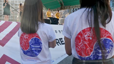 two-female-korean-volunteers-clapping-in-front-of-stage-during-korean-festival