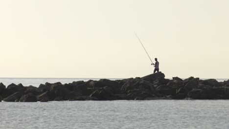 Joven-Pescando-En-El-Mar-Desde-Las-Rocas-Al-Amanecer
