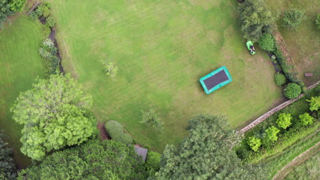 Static-Aerial-Shot-of-Man-Mowing-Lawn-on-Summer’s-Day-using-Ride-On-Lawnmower-from-Birds-Eye-View-Perspective