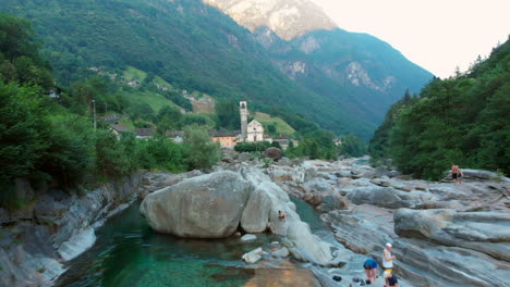 Aerial-revealing-dolly-towards-a-church-over-Verzasca-river,-Switzerland