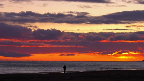 Dramatic-beach-sunrise-with-older-man-silhouetted-against-silver-sea-at-dawn