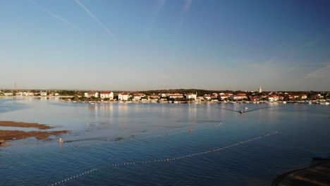 Aerial-panorama-of-a-Nin-town,-Croatia-sandy-beach-and-kids-playing,-with-lagoon-and-boat-approaching-in-sunset