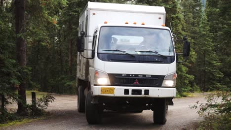 Static-shot-of-a-Mitsubishi-Fuso-turning-a-corner-on-a-dirt-road-in-a-forest-in-Yukon,-Alaska