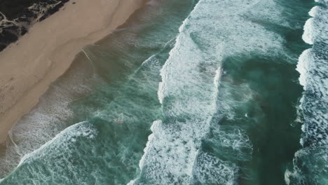 Aerial---Drone-follows-waves-as-they-gently-roll-onto-pristine-beach,-downwards-shot