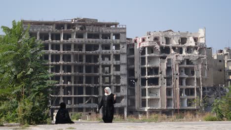 Two-woman-wearing-hijabs-in-Homs-City,-ruined-huge-building-at-the-back