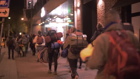 People-carrying-bags-and-camping-gear-walk-the-streets-of-Amsterdam-during-Climate-protests-by-Extinction-rebellion-volunteers-at-night,-early-morning