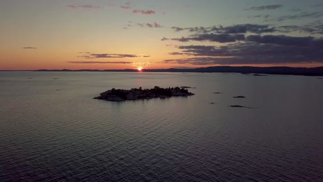 High-View-of-Rocky-Pine-Tree-Island-in-Blue-Lake-at-Sunset,-Drone-Aerial-Wide-Dolly-In