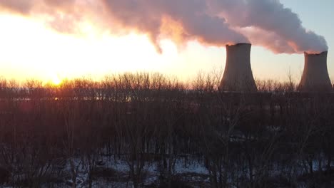 Dolly-up-aerial-drone-shot-of-Nuclear-Power-Plant-Cooling-Towers-at-Sunrise-Sunset-with-Steam-and-Smoke-bright-sun-winter