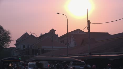 Wide-Exterior-Shot-Of-High-Sun-over-Roof-Tops-at-Dusk-While-There-is-Traffic-In-the-Streets