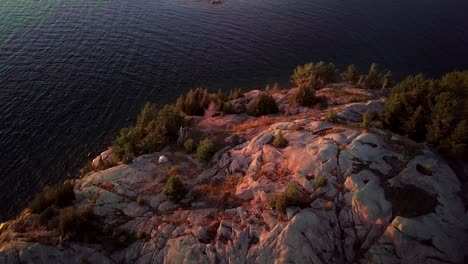 Small-White-Tent-on-Rock-Island-with-Pine-Trees-in-Blue-Lake,-Drone-Aerial-Wide-Pedestal-Down