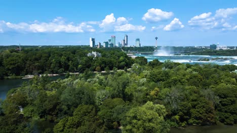 Luftflug-Mit-Spritzenden-Niagara-Wasserfällen,-Fluss-Und-Wunderschöner-Skyline-Im-Hintergrund-An-Sonnigen-Tagen