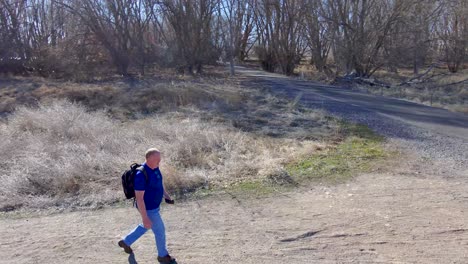 Mature-man-out-for-a-walk-on-a-nature-trail---sweeping-aerial-view-in-slow-motion
