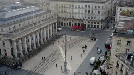 Opera-house-Grand-Theater-square-with-people,-vehicles-and-trolley-tram-tracks,-Aerial-pedestal-rising-reveal-shot