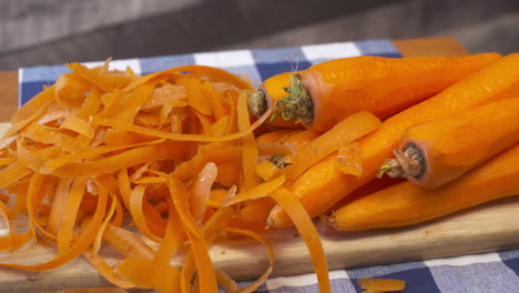 Pile-of-fresh,-whole,-raw,-carrots-and-peels-on-a-cutting-board