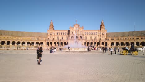 Tilt-down-in-Plaza-de-Espana,-Seville,-with-fountain,-tourists,-and-horse-cart