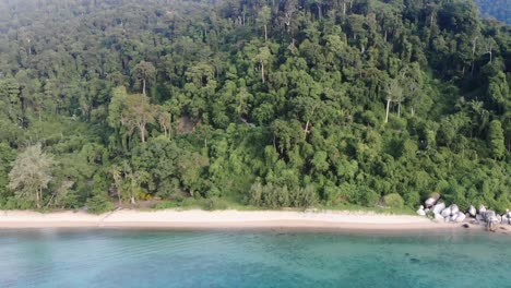 A-drone-video-flying-outward-from-an-empty-Tioman-tropical-island-with-full-of-trees-and-tropical-forest-toward-a-beautiful-blue-aquamarine-ocean-vitamin-sea