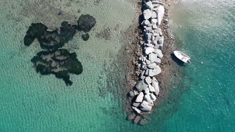 Boat-anchors-on-a-rocky-pier-in-turquoise-water,-aerial-pedestal-shot