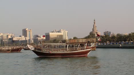 An-Arab-dhow-anchored-in-the-inner-harbour-of-Doha,-Qatar-with-the-iconic-minarate-and-modern-Doha-skyline-in-view