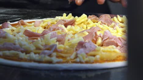 Nahaufnahme-Von-Hand,-Die-Pizza-Mit-Schinken-Und-Käse-Belegt